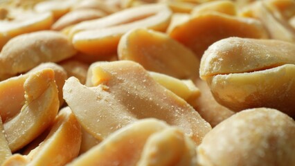 Golden-brown peanuts, split open, expose their creamy kernels beneath a delicate salt dusting. Their rough texture hints at the satisfying crunch within.
