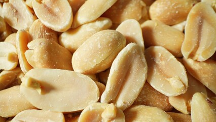 A meticulous examination reveals roasted peanuts, each halved, displaying a consistent golden-brown hue. The surface, lightly slick with oil, denotes the meticulous roasting process.
