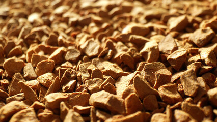 In the intimate close-up of freeze-dried coffee, warm light dances, casting gentle shadows, revealing a mesmerizing mosaic of golden-brown fragments, reminiscent of rugged gemstones.
