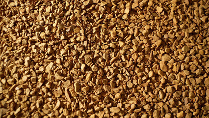 Up close, freeze-dried coffee granules reveal a rough, uneven surface, tinted in tones of brown....