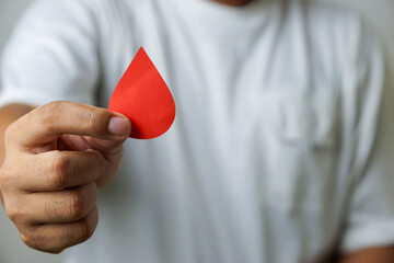 a man's hand holds a drop of donor blood with white background. world blood donor day concept,...