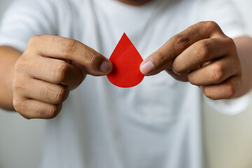 a man's hand holds a drop of donor blood with white background. world blood donor day concept,...