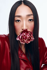 Seductive woman with black hair wearing red leather jacket and flower in mouth posing for camera