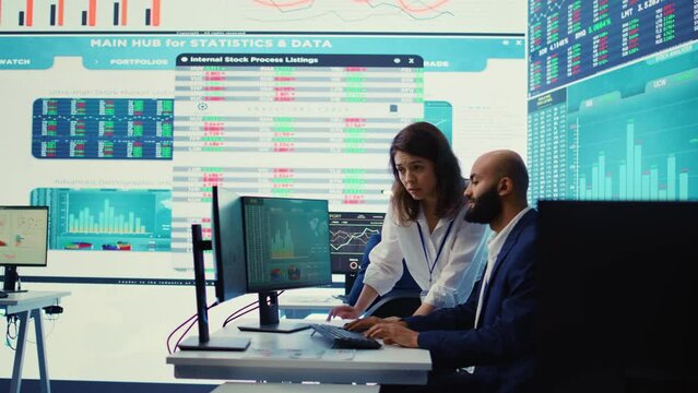 Teammates examining statistics and infographics on computer in control room, joining forces to gather insight for business development. Analysts discussing legal changes. Camera B.