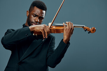 African American male musician in a black suit playing the violin against a gray background