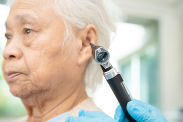 Audiologist or ENT doctor use otoscope checking ear of asian senior woman patient treating hearing...