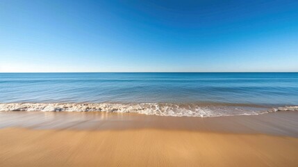 Fototapeta premium A serene beach with golden sand meeting the calm blue sea under a clear sky, ideal for vacation and travel visuals.
