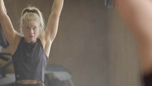 Strong female athlete doing clean and jerk weightlifting checks form in mirror