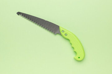 Close-Up of Hand Saw with Green Handle on Light Green Background