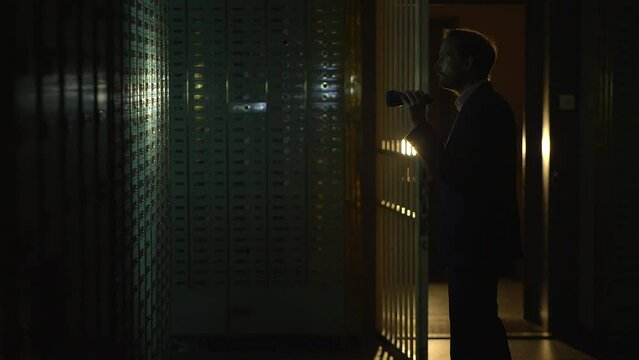 Man in suit spies Investigating vault safe holding a flashlight in dark room