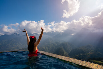 Young woman traveler relaxing in sky pool and looking at the beautiful nature landscape with blue...