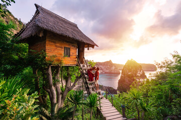 Young couple traveler enjoying and looking beautiful sunrise at the tree house in Nusa Penida island Bali, Indonesia