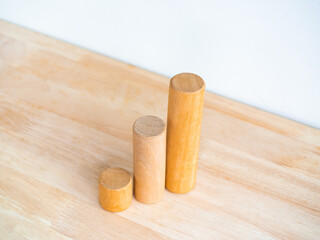 Three size of simple cylindrical wooden sticks as a business chart steps on wood desk on white background. Eco business growth graph process, goal steps, success, and economic improvement concepts.
