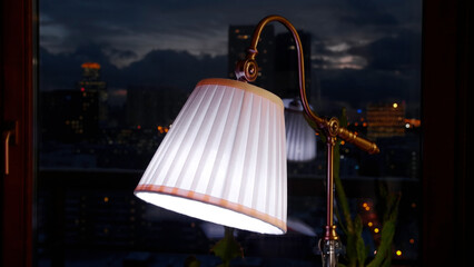 The lamp in the living room in front of window. Creative. Lamp on the table and evening city sky on...