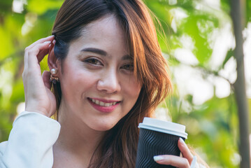 Woman drinking coffee hands holding hot disposable cup in green park. Happy Relax beautiful asian woman smiling face standing outdoors garden. Young women enjoy nature morning Freedom Lifestyle.