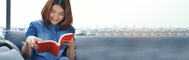 Banner Relax asian woman reading book sitting on sofa in living room holding book. Banner Young...