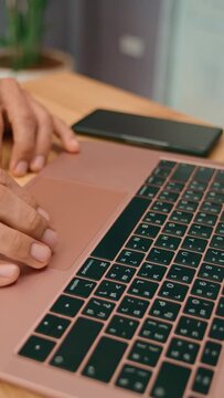 In a professional office setting, hands are seen typing on a laptop with a smartphone on the desk