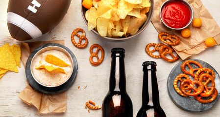 Snacks for watching an American football game. Beer, chips, pretzels, sauce on wooden background