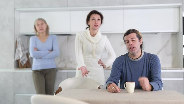 Elderly mother and woman scold swear at man. Male is upset because of family conflict, dejectedly listens to his wife and mother scolding him. Complex intergenerational relationships 