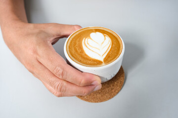 A cup of hot latte coffee on the table for breakfast. Hand in frame