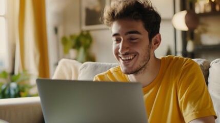 Young man smiling while using laptop in cozy living room during daytime.