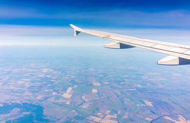 Fototapeta premium Aerial view from airplane window above green ground. View from the airplane window with beautiful clouds at sunrise
