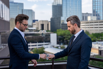 Businessman giving money to his partner outdoor. Businessman giving money. Teamwork. Business partnership. Rich businessman in suit with money dollar bills. Giving money concept. Offering for business
