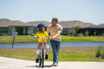 Father and son riding bike on a park. Child in safety helmet with father riding bike on summer day. Father teaching son riding on bike. Child son in bike helmet and father on bicycle. Fathers day.