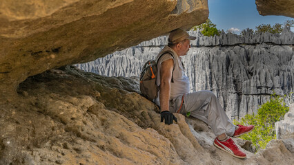 A tired man with a backpack is resting while climbing. A tourist is sitting in a crevice of rocks....