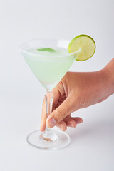 Hand holding glass of Classic Margarita cocktail decorated with sliced lemon, mint leaves and salt...