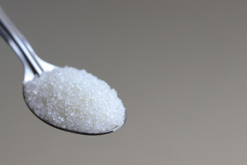 Close up of sugar in steel spoon with plain background.