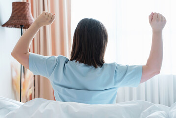 Young woman goes to window and stretches his arms, rear view.