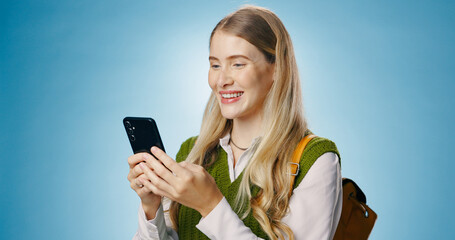 Fototapeta premium Girl, phone and backpack in studio for education, learning or reading information of college results. Young person or student typing and scroll on mobile app for class schedule on blue background