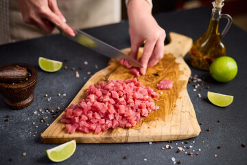 Woman cut tuna steak into slices on a wooden cutting board at domestic kitchen