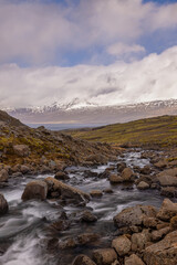 Landschaft mit einem Wasserfall, im Hintergrund Berge mit Schnee