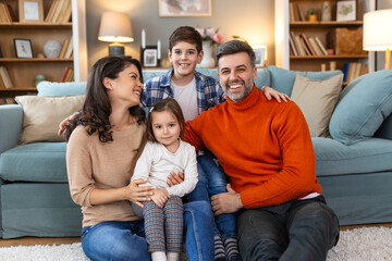 Happy family having fun at home, parents and little children sit on sofa together, Happy family sitting on sofa laughing together. Cheerful parents playing with their kids at home.