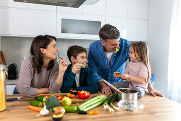 Overjoyed young family with son and daughter have fun cooking diner or lunch at home together, happy smiling parents enjoy weekend play with small children doing cooking in kitchen