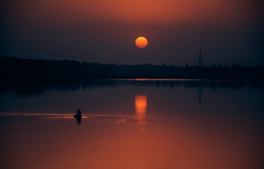 majestic evening view at Baranti lake (a popular travel spot in Purulia), with holden hued last rays of setting sun creating a magical backdrop. A lone person on floating raft seen fishing in water.