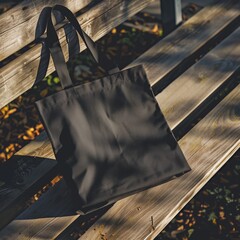 Trendy mockup template of a black tote bag rests on a wooden bench, illuminated by warm sunlight, creating contrasting shadows and textures.