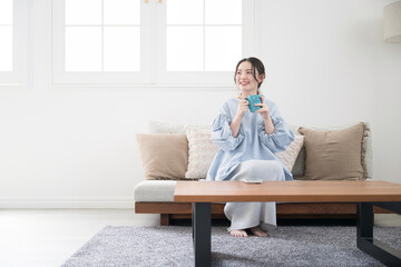 コーヒーや飲み物を持ってリビングでくつろぐ女性　広角