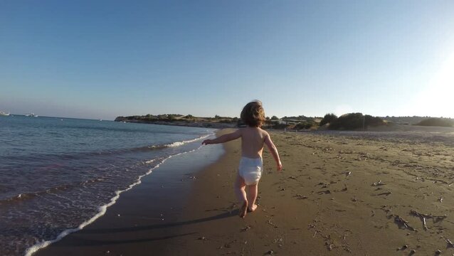  Slow motion of toddler baby girl in nappy running on sandy beach  through sea waves