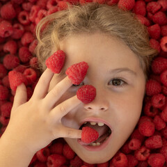 Kid eating raspberries. The kids face with raspberries fruit and berries. Summer, pink red raspberry background.
