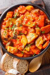Vegetable gyuvech eggplants, peppers, tomatoes, onions, carrots, fresh greens closeup on the bowl on the table. Vertical top view from above