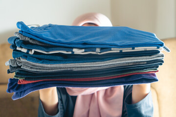 woman with hijab holding a stack of clothes that has been ironed