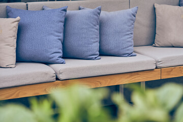 Outdoor patio with sofa and cushions. A blurred green plant in an outdoor garden. Sofa with copy...