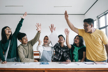 Group Of Young Asian Diversity Friends Raising Hands Together Celebrating Achievement In Classroom