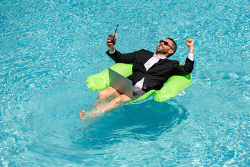 Successful business man in suit in pool water. Business man in suit working on laptop in swimming pool. Travel tourism and business concept. Crazy male office business employee using laptop.