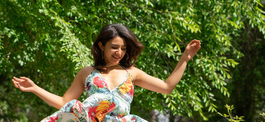 Latin woman wearing a flower dress jumping in nature happy. Free lifestyle