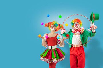 Funny juggler female clown juggling balls in the circus, man entertainer as Joker in suit and wig, with clown whiteface makeup looking through hula hoop. Professional actors at events © TSViPhoto