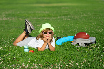 Summer holiday with children. Child playing in garden. Happy little boy lying on the grass at the spring day.